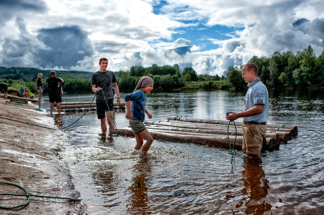 Familj leker vid sjö med flottar av trä